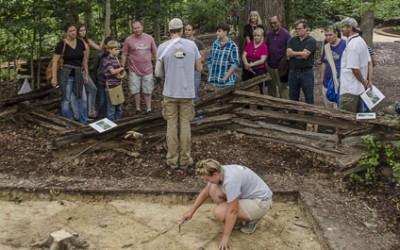 Crew Chief Joe Downer explains the goals of the Slave Cemetery Survey to the public while Leah Stricker uncovers a burial.